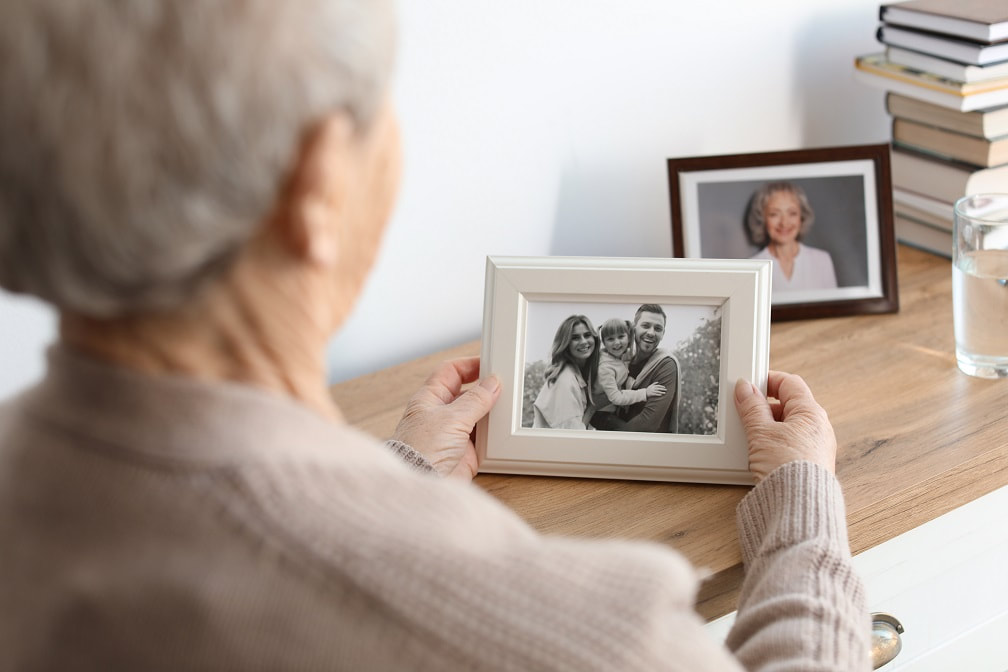 loneliness pandemic - social isolation - elderly woman looking at family pictures